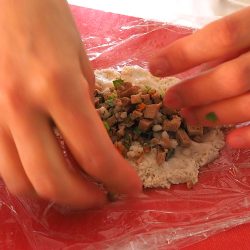 手順8：6で使ったラップに生地をスプーンですくって広げる。約大さじ1の餡をのせ、ラップで茶巾絞りのように包む（具は多少余る）。ベーキングシートの上にのせる。